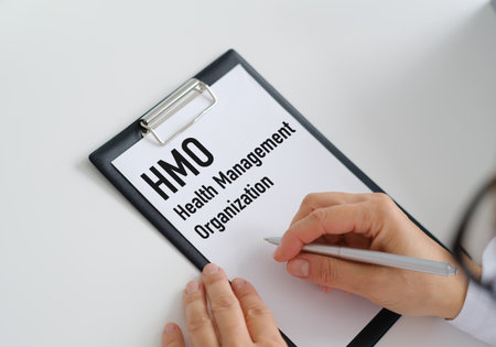 A person is writing on a clipboard that says Health Management Organization. The clipboard is on a...