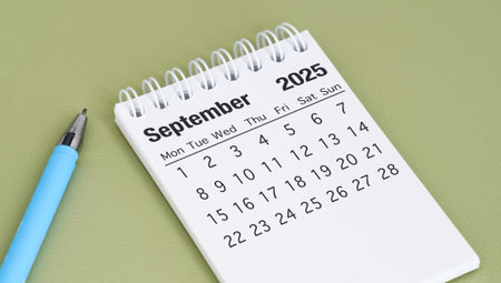 A blue pen sits next to a calendar that says September 2025. The pen is on a green surface