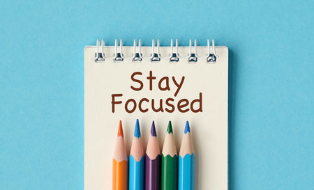 A notebook with a spiral binding and a pencils on top of it. The pencils are in different colors and...