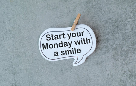 A white sign with a black lettering that says Start your Monday with a Smile. The sign is hanging on...