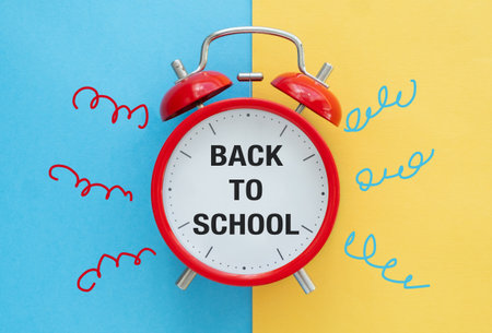 A red alarm clock with the words Back to School written on it. The clock is surrounded by colorful...