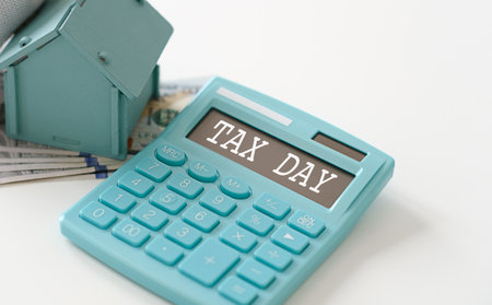 A blue calculator with the word tax on it. A house and some money are on the table