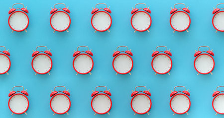 A row of red alarm clocks are placed on a blue background. The clocks are all the same size and shape, and they are all facing the same direction. Concept of monotony and repetitionの写真素材