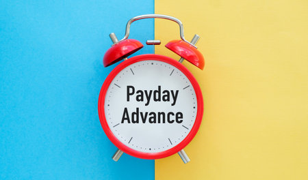 A red alarm clock with the words Pay day Advance written on it. The clock is set to the timeの写真素材