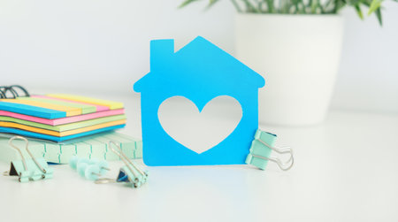 A blue house with a heart cut out of it sits on a table. The house is surrounded by colorful sticky notes and a potted plant. Concept of warmth and comfort, as the heart shapeの写真素材