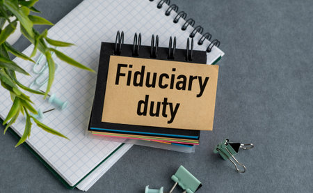 A notebook with a piece of paper that says Fiduciary Duty on it. The notebook is on a table with a...