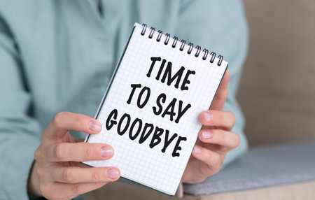 A person holding a spiral bound notebook with the words Time to Say Goodbye written on itの写真素材
