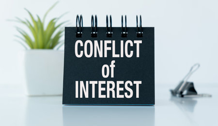 A black notebook with the word Conflict of Interest written on it. The notebook is sitting on a table with a potted plant in the backgroundの写真素材