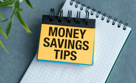 A yellow sticky note with the words Money Saving Tips written on it. The note is placed on top of a...