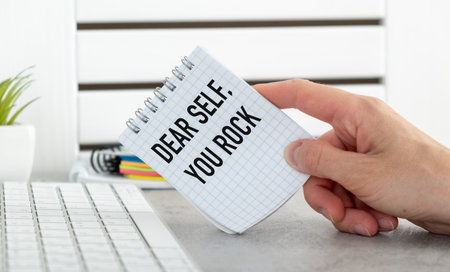 A person is holding a piece of paper that says Dear Self, you Rock The paper is folded in half and...