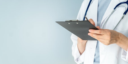 A doctor is holding a clipboard and writing on it. The clipboard is black and the doctor is wearing a white coatの写真素材