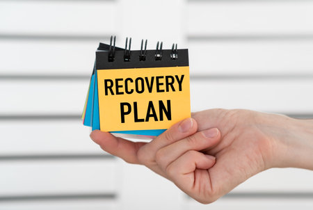 Hand holding open notebook with text Recovery Plan on light backgroundの写真素材