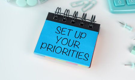 A blue notebook with the words Set Up Your Priorities written on it. The notebook is on a table with...