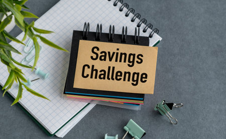 A notebook with a Savings Challenge written on it. The notebook is on a table with a pair of scissors and a plantの写真素材