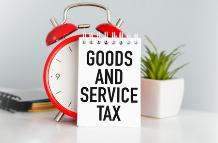 A red alarm clock with a sign that says Goods and Service Tax on it, business conceptの写真素材