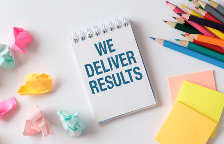 WE DELIVER RESULTS Text written on notepad with office tools and documents.の写真素材