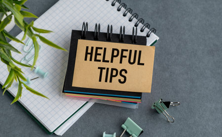 A notebook with a sign that says Helpful Tips on top of it. The notebook is on a table with a pair of scissors and a pair of paper clipsの写真素材