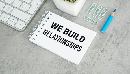 A white notebook with the words We Build Relationships written on it. A blue pencil is on the table...