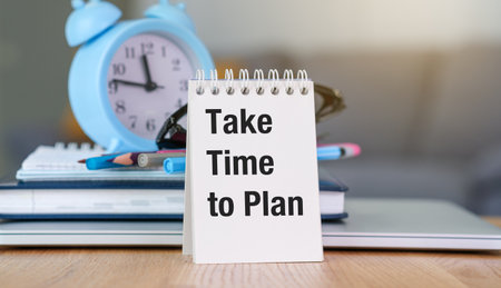 A blue clock sits on a table next to a white planner that says Take time to Plan.