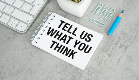 Tell Us What You Think writing on a sheet of notebook with pencil, keyboard on a gray table