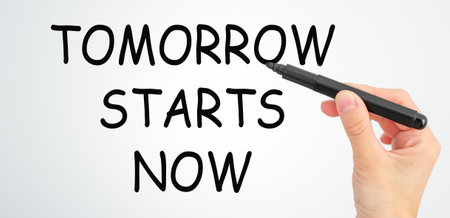A hand is writing the word Tomorrow Starts Now on a white background. Concept of motivation and...