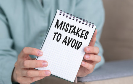 A person is holding a spiral bound notebook with the words Mistakes to Avoid written on it