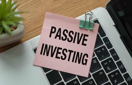 A pink note with the word Passive Investing written on it is clipped to a laptop keyboard. The note...