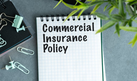 A notebook with the word Commercial Insurance Policy written on it. The notebook is on a table with a pair of scissors and a plantの写真素材