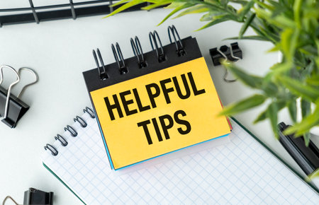 A yellow sticky note with the word Helpful Tips written on it. The note is placed on top of a white notebookの写真素材