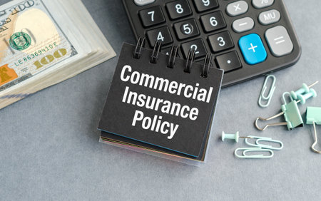 A calculator sits on a desk with a stack of money and a piece of paper that says Commercial Insurance Policyの写真素材