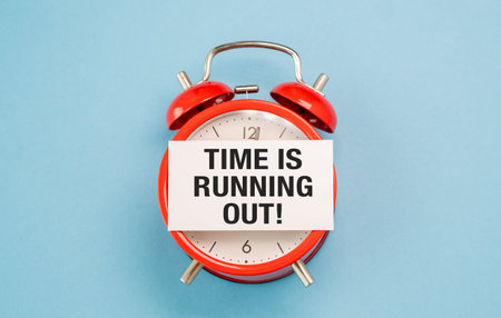 A red alarm clock with a white paper that says Time is Running Out textの写真素材