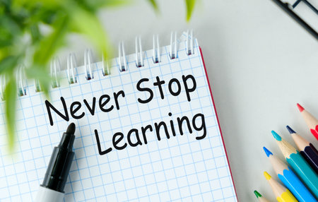Never Stop Learning is written on a spiral bound notebook. The notebook is sitting on a table with a pencil and a markerの写真素材