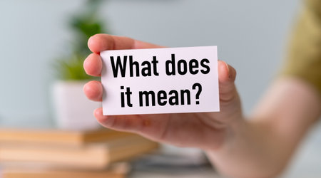 A person is holding a white card that says What Does it Mean. Concept of curiosity and contemplation, as the person is holding the card and pondering its meaningの写真素材