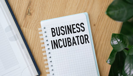 A notebook with the word Business Incubator written on it. The notebook is on a table with a plant next to itの写真素材