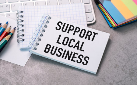 A white piece of paper with the words Support Local Business written on it. The paper is sitting on a desk with a keyboard and a pencilの写真素材