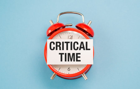 A red alarm clock with the words Critical Time written on a white piece of paper. The clock is set to the time ofの写真素材