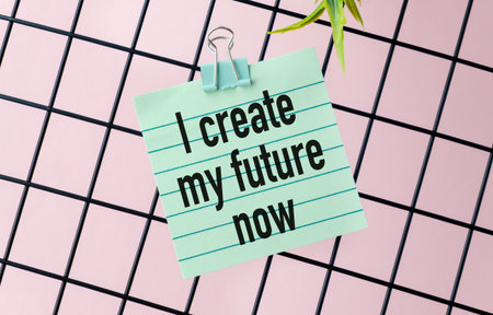 A green piece of paper with the words I Create my Future Now written on it. The paper is clipped to...