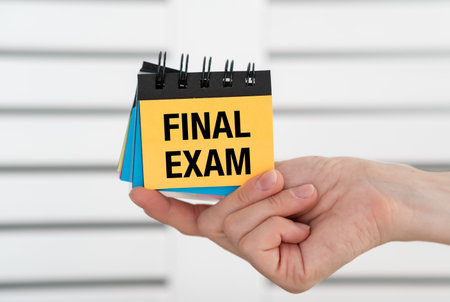 Final Exam text on an open notebook in hand on a light backgroundの写真素材