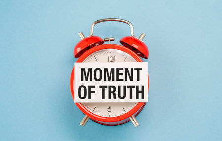 A red alarm clock with the words Moment of Truth written on a white piece of paper. The clock is set to the time ofの写真素材