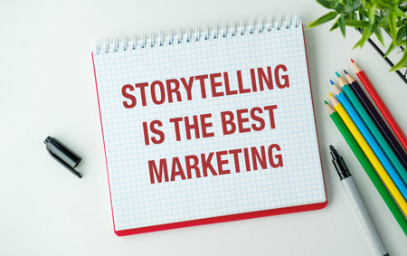 A red spiral notebook with the words "storytelling is the best marketing" written on it. The notebook is placed on a table with a pen and a set of colored pencilsの写真素材