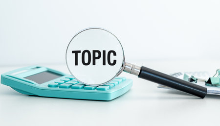 A calculator sits on a table with a magnifying glass over the word TOPIC. The magnifying glass is black and the calculator is greenの写真素材