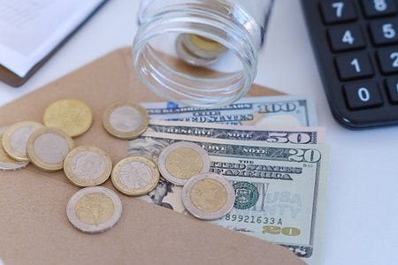 A jar of coins and a stack of bills are on a table. The jar is half full and the coins are scattered around it. The bills are stacked neatly on top of each other. Concept of financial responsibilityの写真素材