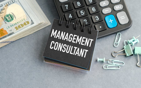 A calculator sits on a desk with a stack of money and a piece of paper that says Management Consultantの写真素材