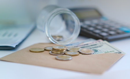 A jar of coins and a calculator are on a table. The jar is half empty and the calculator is on top...