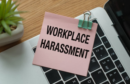 A pink piece of paper with the word Workplace Harassment written on it. The paper is clipped to a laptop keyboardの写真素材