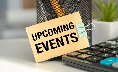 A small sign that says Upcoming Events is sitting on top of a calculator. The calculator is black...