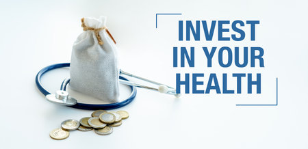 A bag of coins and a stethoscope are on a white background with the words Invest in Your Health written belowの写真素材