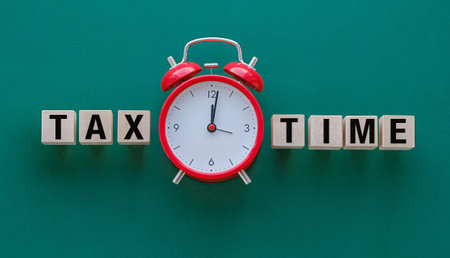 A red alarm clock with the word Tax Time written in black letters. The clock is set to the time