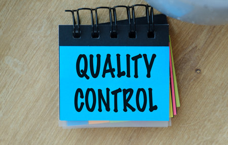 A blue notebook with a yellow and green strip on it that says Quality Control. The notebook is on a wooden tableの写真素材