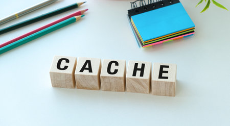 A wooden block with the word Cache written on it. The block is on a table with a pencil, a pen, and a notebookの写真素材